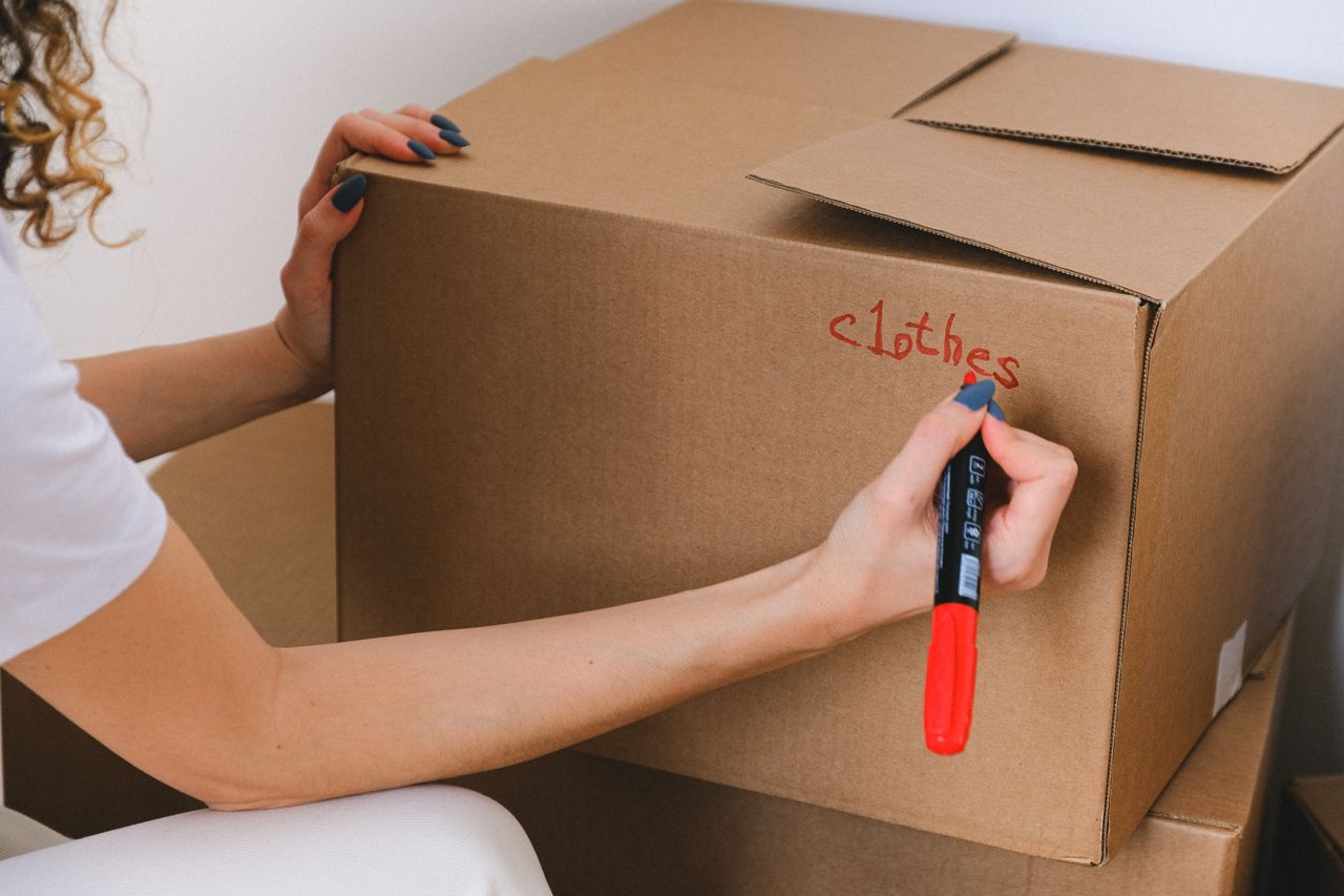 Gros plan d’une femme étiquetant une boîte en carton avec un marqueur rouge à l’intérieur.